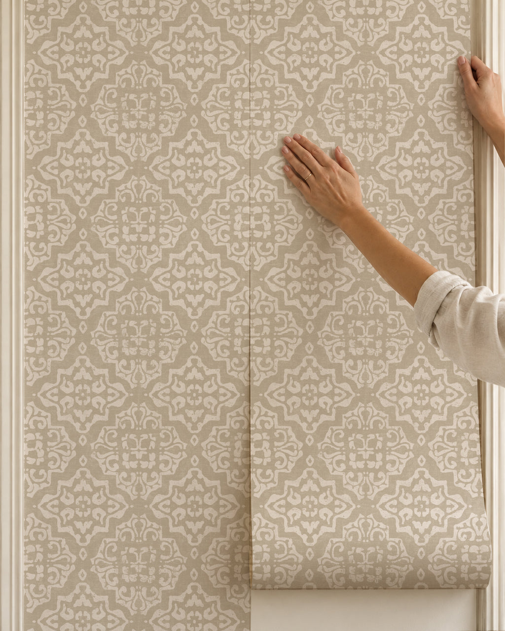 Antique ornamental damask wallpaper in taupe and cream being applied to a wall.