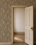 Botanical fern wallpaper in taupe and cream in a room with an open wooden door.
