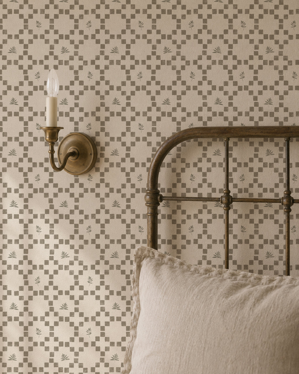 Botanical lattice olive on cream wallpaper in cozy bedroom with metal bed and wall sconce.
