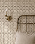 Botanical lattice olive on cream wallpaper in cozy bedroom with metal bed and wall sconce.