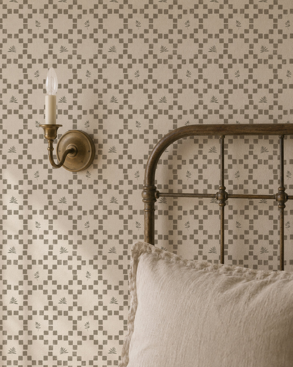 Botanical lattice olive on cream wallpaper in cozy bedroom with metal bed and wall sconce.