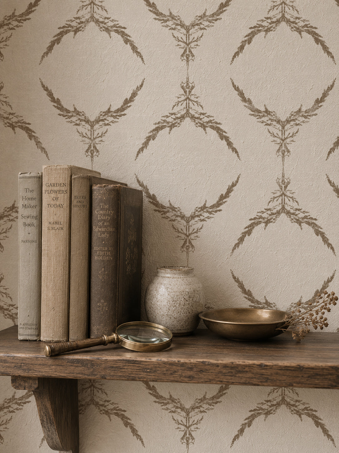 Botanical taupe on cream wallpaper with books and decor on a wooden shelf.