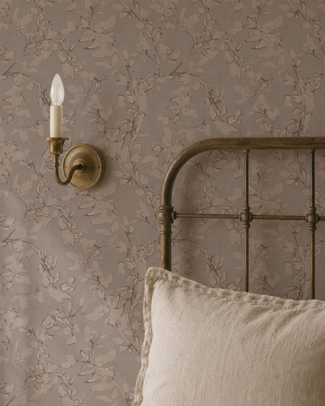 Brown floral vine wallpaper in vintage bedroom with metal bed and wall sconce.