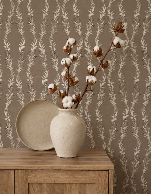 Brown floral vine wallpaper in rustic room with vase and wooden cabinet.