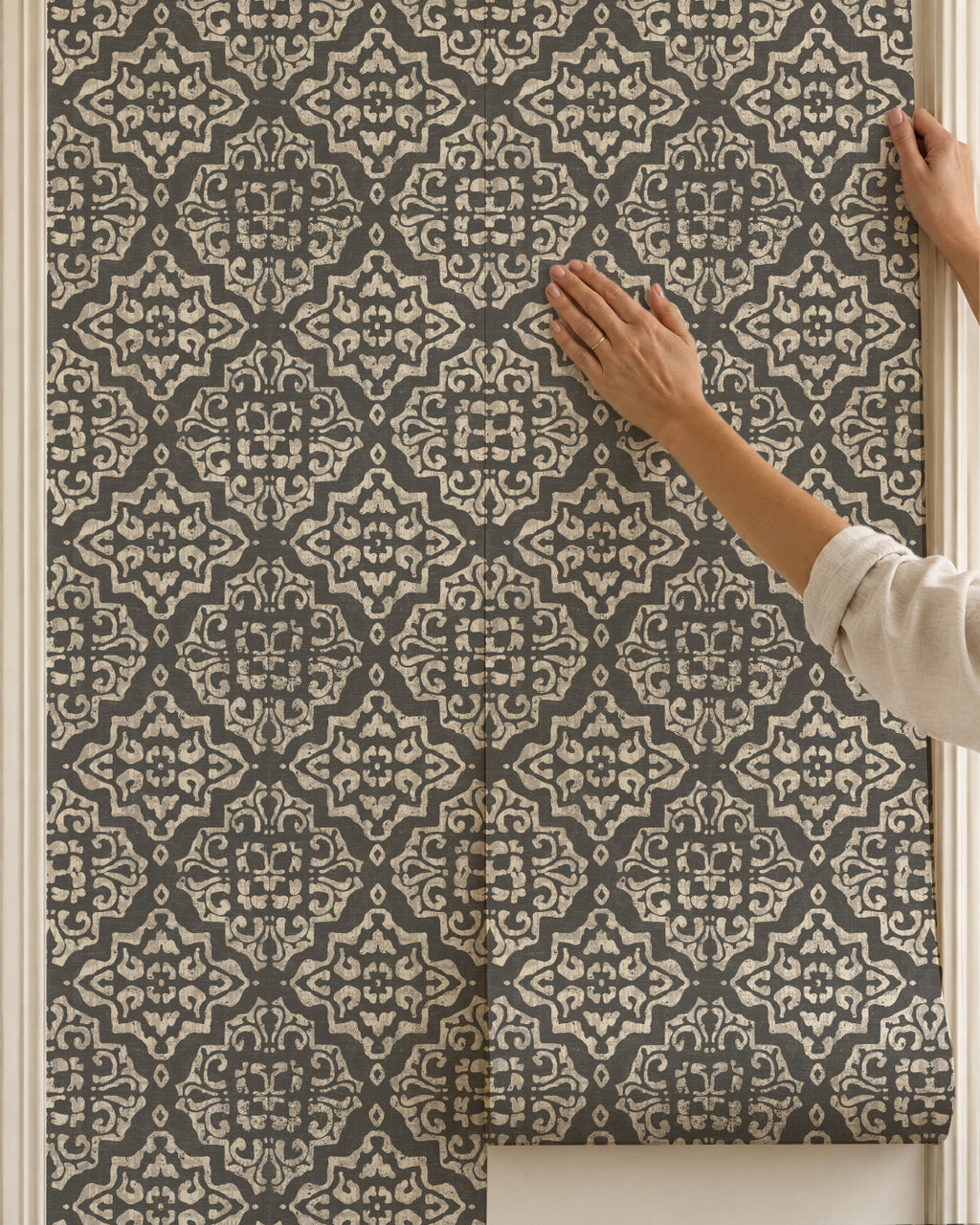 Charcoal and cream damask wallpaper with ornate motifs being applied to a wall.