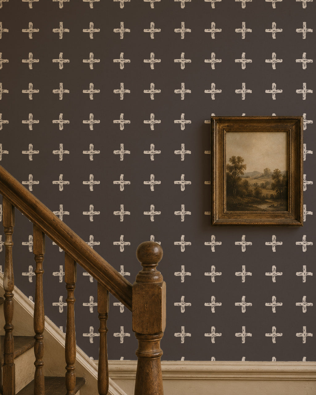 Cream cross pattern on charcoal wallpaper in hallway with wooden staircase and framed art.