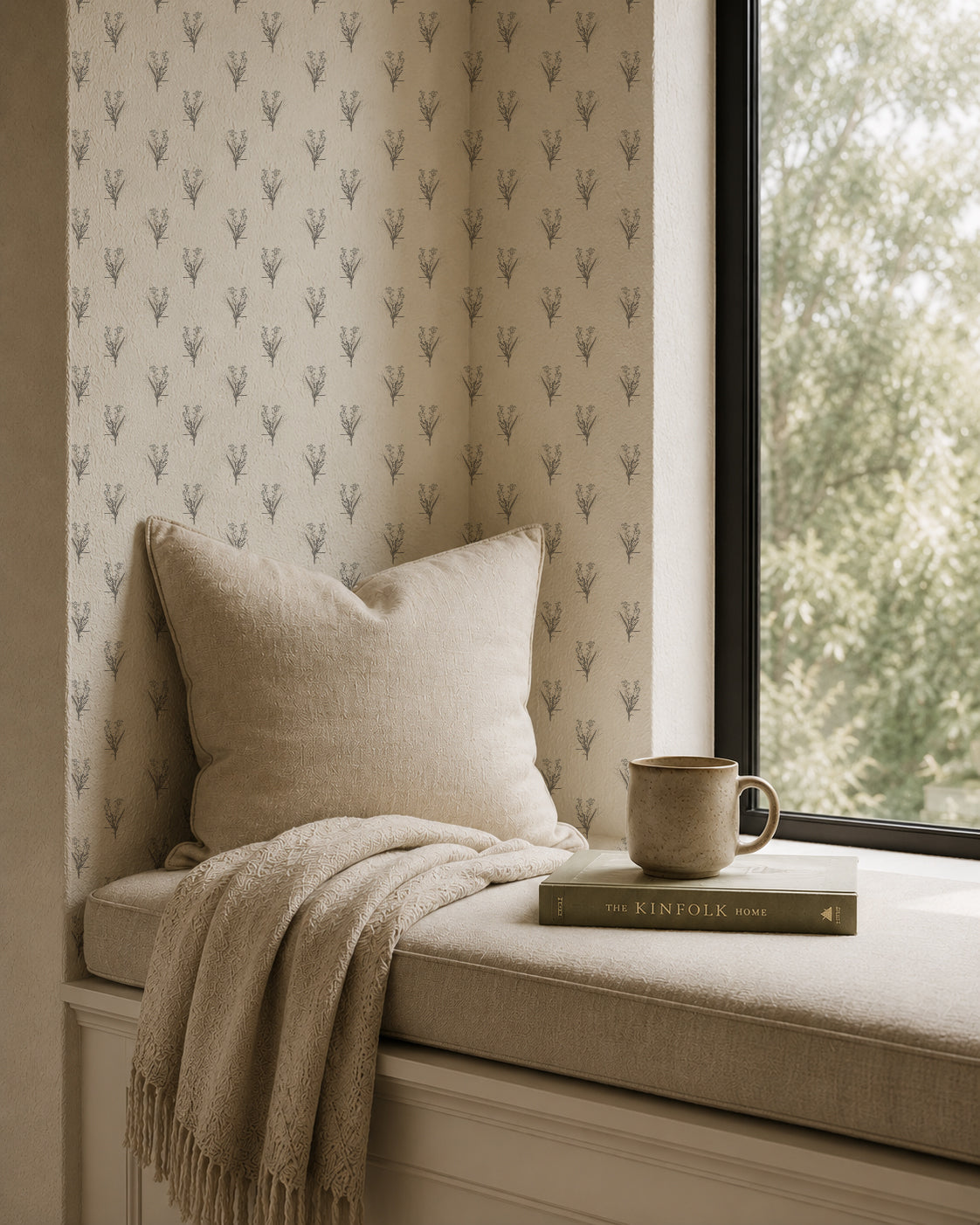 Cream floral wallpaper with grey motifs in cozy window nook with pillow and book.