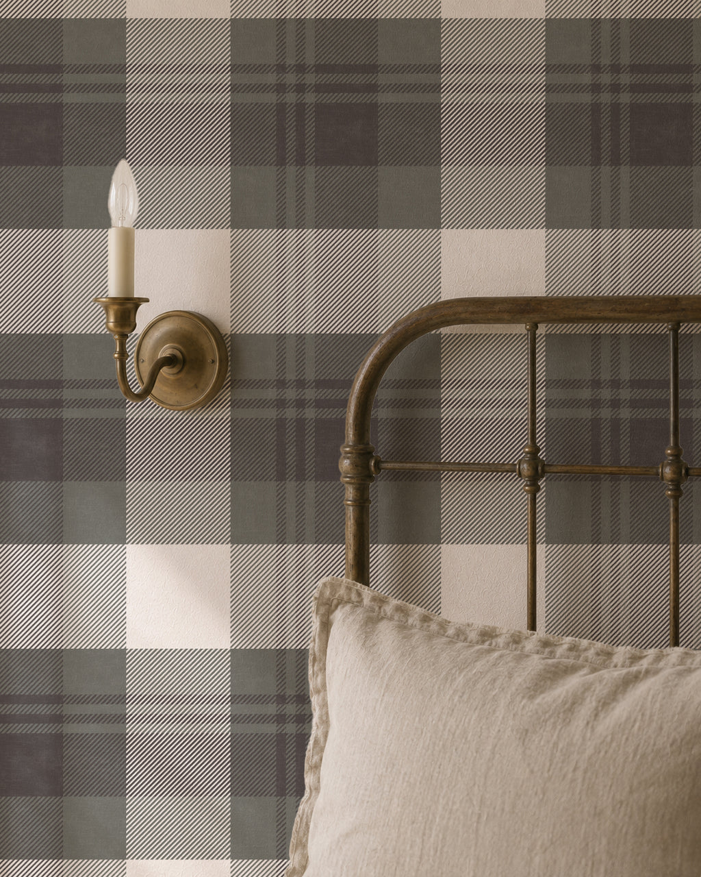 Green and charcoal plaid wallpaper in rustic bedroom with metal bed and sconce.
