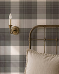 Green and charcoal plaid wallpaper in rustic bedroom with metal bed and sconce.