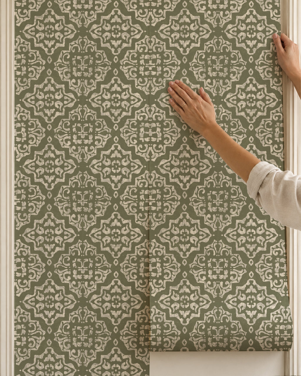 Ornate moss damask wallpaper with cream motifs being applied to a wall.