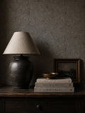 Navy ochre floral vine wallpaper in cozy room with lamp and books.