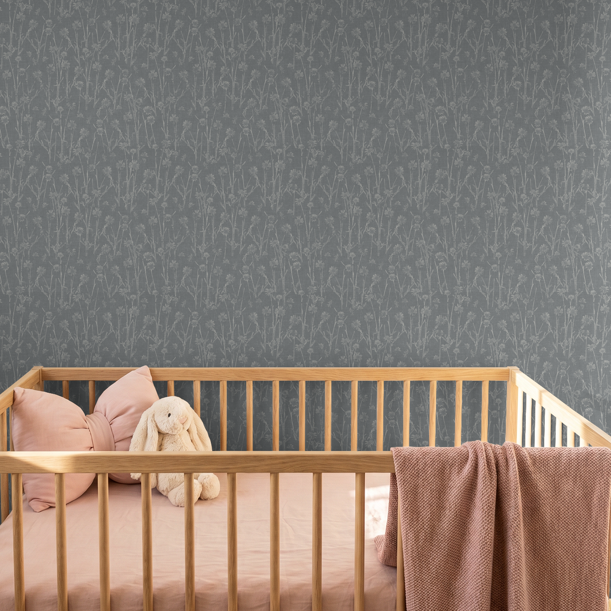 Navy wildflower patterned wallpaper in a nursery with wooden crib and pink bedding.