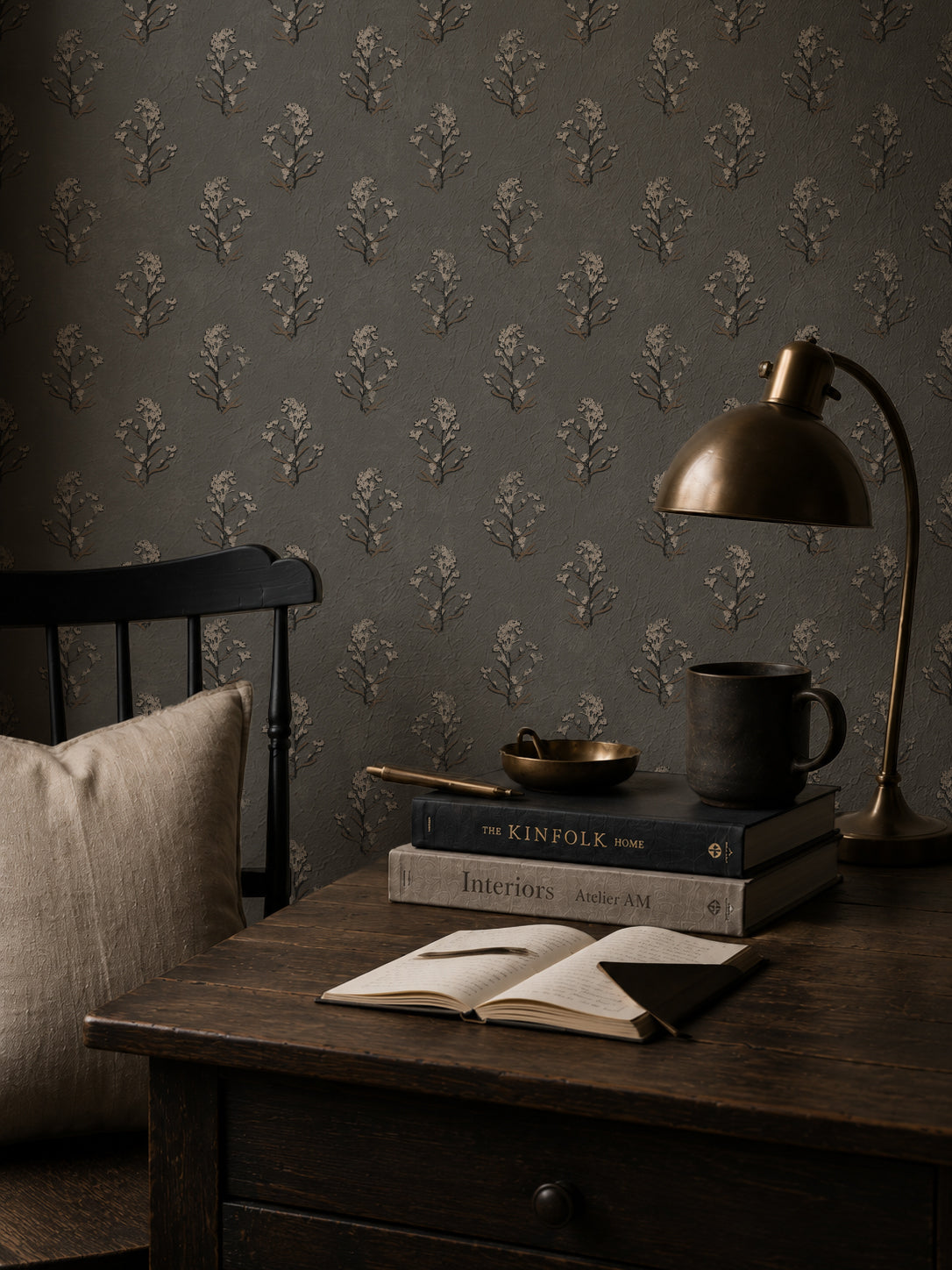 Slate floral wallpaper with white blossoms in a cozy reading nook with books and lamp.