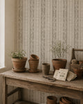 Taupe botanical stripe wallpaper in rustic room with potted plants and wooden table.
