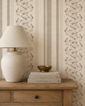Taupe floral stripe wallpaper in cozy room with wooden table and lamp.