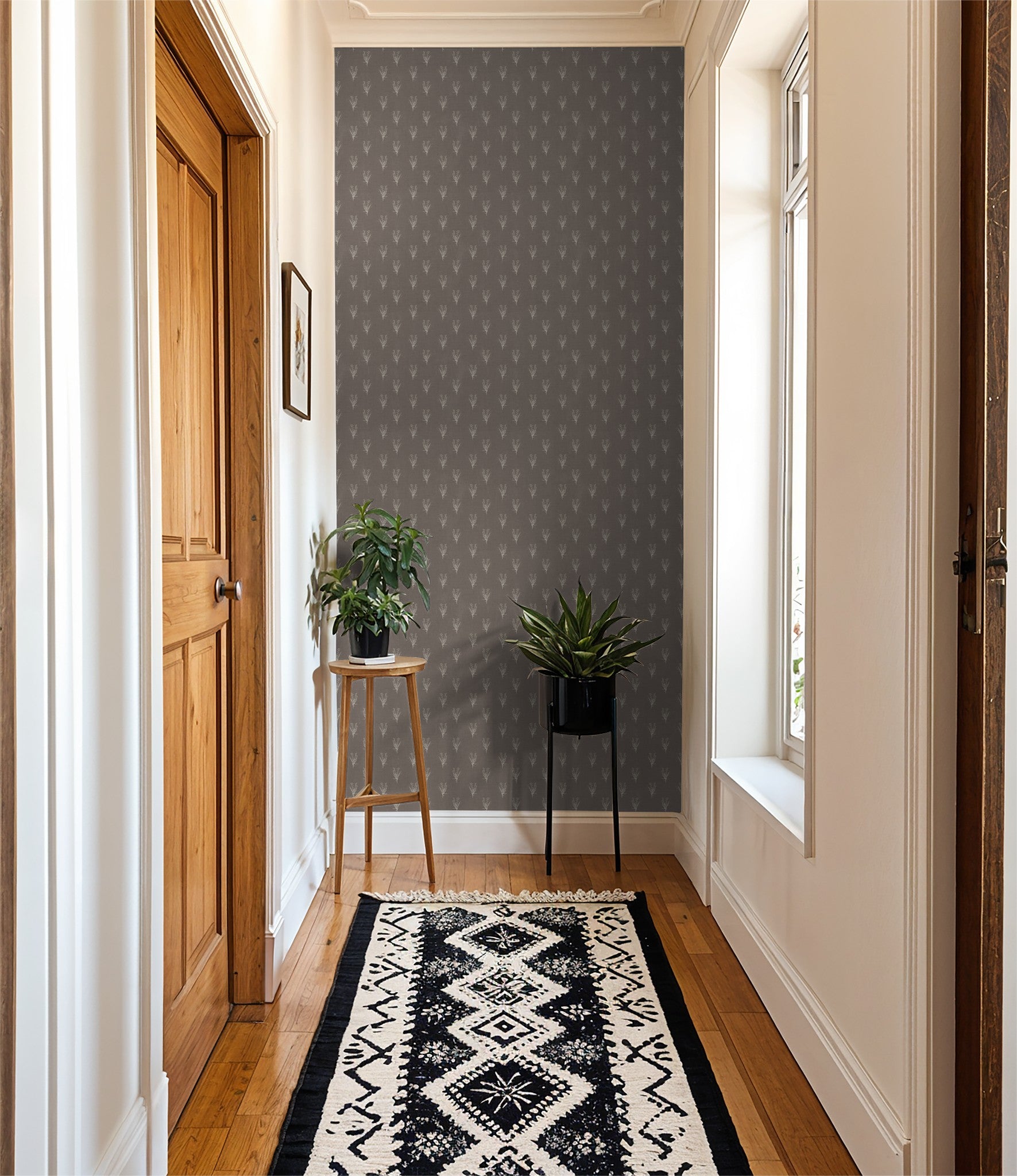 Hallway with taupe floral wallpaper, wooden floor, plants, and patterned rug.
