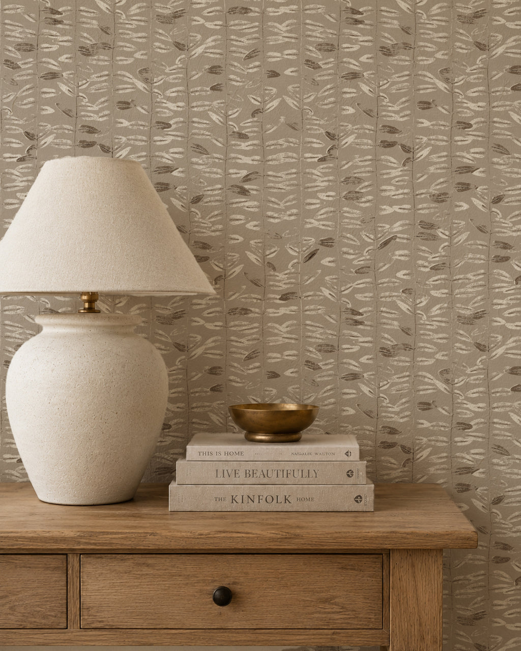 Taupe olive branch wallpaper in rustic room with lamp and books.