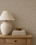 Taupe wallpaper with vine pattern in cozy room with wooden table and lamp.