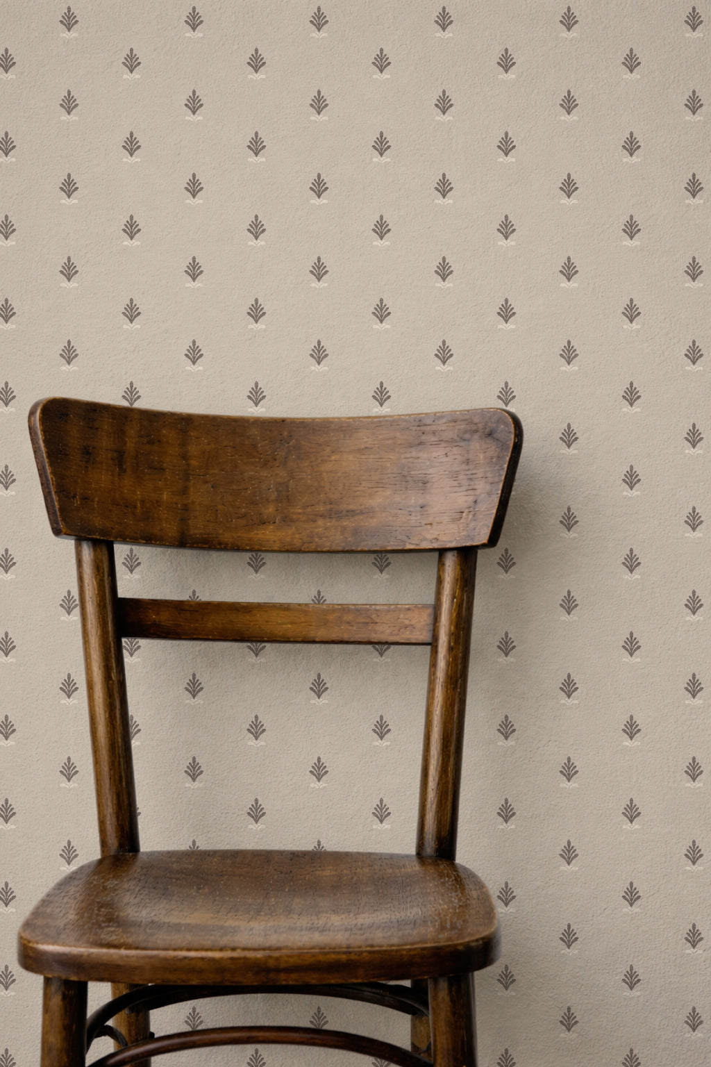 Vintage block print wallpaper with taupe backdrop and ornate motifs behind wooden chair.